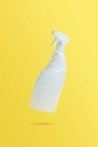 Levitation, flying blank toilet or window cleaner bottle with sprayer. Isolated on yellow background. White plastic packaging. Household chemistry. Falling in air single object. Detergent with trigger