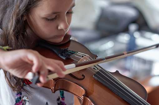 A seven-year-old girl with high abilities is very serious and focused as she rehearses at home with her violin. Selective focus.