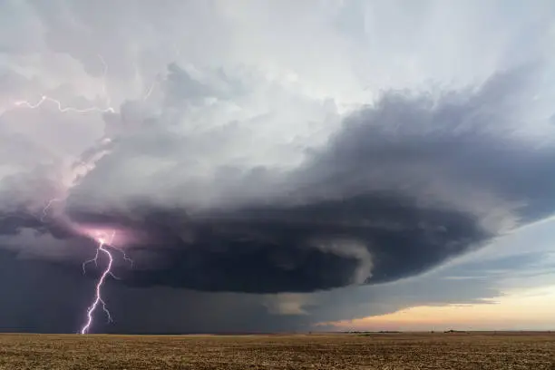 Dramatic supercell thunderstorm clouds with a lightning bolt strike over a field in Kansas.