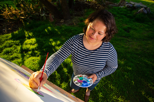 Woman who enjoys her life in her 40's, painting in the garden of her house.