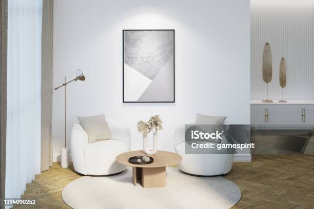 Modern Interior With An Illuminated Vertical Poster On A White Wall The Decor On A Coffee Table Two Modern Chairs A Lamp Near A Curtained Window Decor On A Nightstand In The Background Stock Photo - Download Image Now