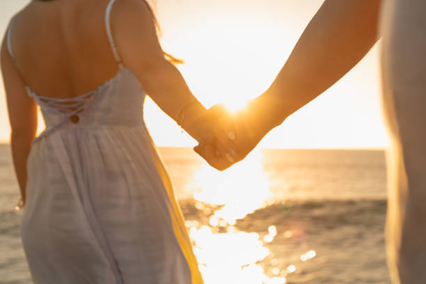 Romantic couple holding hands on the beach at sunset. Love and relationship concept.