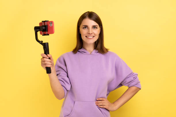 istock Delighted woman using cell phone and steadicam for broadcasting livestream, keeping hand on hips. 1394110775