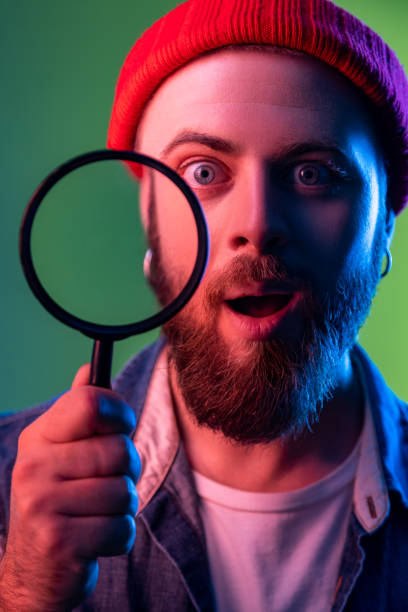 istock Man standing, holding magnifying glass and looking at camera, having astonished surprised face. 1394111437