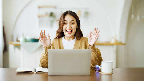 istock Smiling asian young woman working on laptop at home office. Young asian student using computer remote studying, virtual training, e-learning, watching online education webinar at house 1394113953