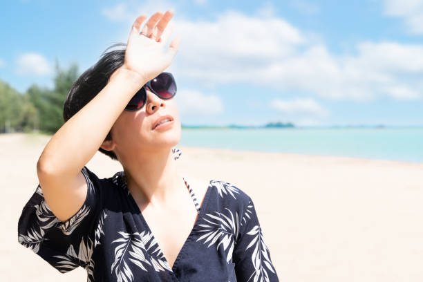 hermosa mujer asiática levanta la mano para bloquear la luz del sol en la playa - luz ultra violeta fotografías e imágenes de stock