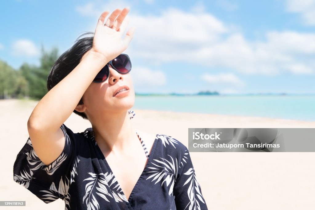Beautiful Asian woman raise hand to block sunlight at the beach Beautiful Asian woman with sunglasses look up and raise hand to block sunlight at the beach Sunburned Stock Photo