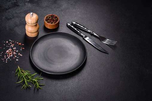 Empty gray plate on a dark background with a knife and fork