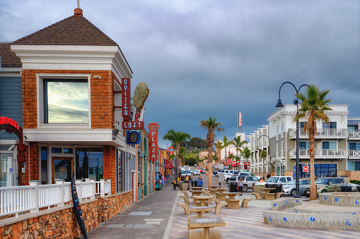 Pismo Beach, California, USA - March 3, 2022.  Pismo Beach Pier plaza at sunset. Shops, restaurants, walking people, downtown of city, city life