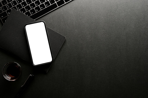 Dark office desk top view with smartphone white screen mockup, office accessories and copy space.
