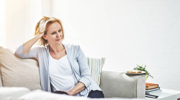istock Happy mature woman looking thoughtful while relaxing on a sofa alone at home 1394124266