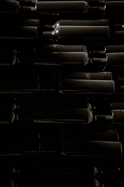 Black and white low light image of unlabelled dusty wine bottles in wire cages