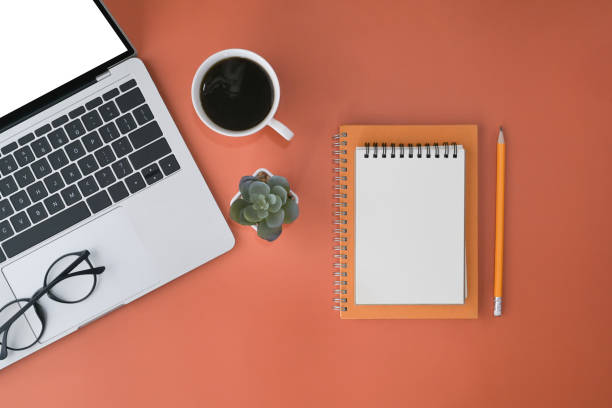 istock Top view computer laptop, coffee cup, notebook and glasses on orange background. 1394132986