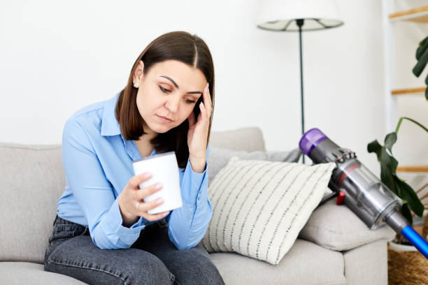 istock Upset depressed brunette lady wearing blue shirt touching head, sitting on sofa, looking down, feeling worried and stressed about the future and thinking about own problems 1394133040