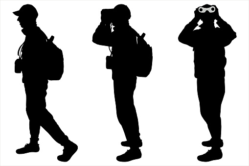 Man, the boy in a hat, climber with a backpack on his back standing, looking through binoculars. Tourist with the binoculars in hands. Orientation to districts. Male silhouette. Side view, full face.