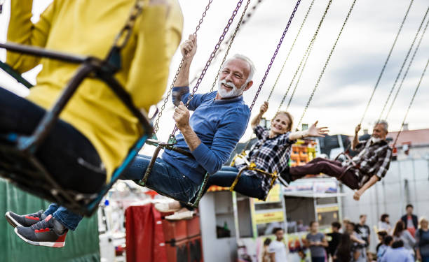 istock Happy senior friends having fun while riding on chain swing at amusement park. 1394136696