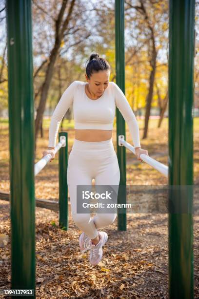 Asian Woman In Casual Sports Clothes Working Out On Parallel Bars In Public Park Stock Photo - Download Image Now