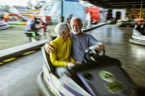 istock Happy senior couple talking while driving bumper car at amusement park. 1394138025