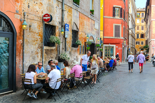 Rome, Italy, June 04 -- Some customers enjoy life and the Italian cuisine sitting outside a lovely restaurant and bistro along Via dei Coronari, near Piazza Navona, in the historic and baroque heart of the Eternal City. Called Via Recta in medieval times, Via dei Coronari is still today one of the main pedestrian routes to St. Peter's Basilica from the center of Rome and from the Piazza Navona area. The Rione Parione, the district surrounding Piazza Navona, is one of the most beautiful and visited districts of Rome for the presence of countless artistic and historical treasures, monuments and ancient Romanesque and Baroque churches, but also for its squares and hidden alleys to explore freely, where it is easy to find typical restaurants, small artisan shops, street artists, and the original Roman soul. In 1980 the historic center of Rome was declared a World Heritage Site by Unesco. Image in high definition format.