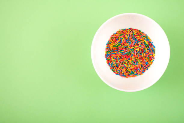 spruzzi di zucchero colorati su una pentola bianca su sfondo verde. - biscuit red blue macro foto e immagini stock