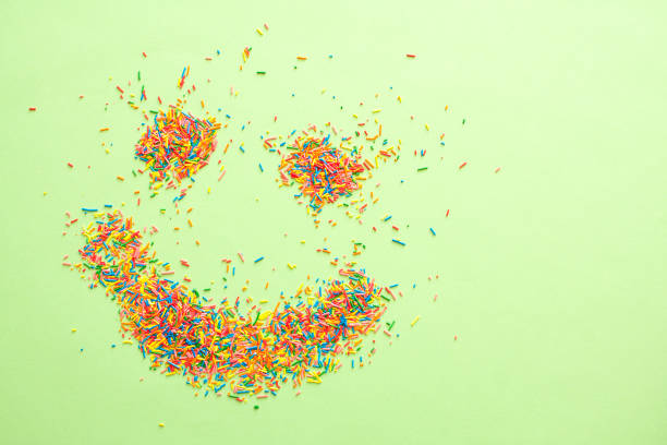 emoji sorridente feito de doces polvilhos coloridos de açúcar em fundo verde com espaço livre de cópia. - cupcake sprinkles baking baked - fotografias e filmes do acervo