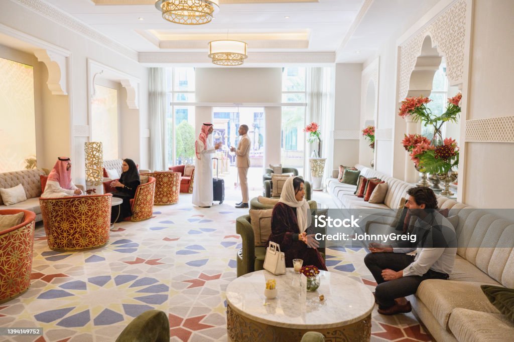 Riyadh hotel guests enjoying conversation in tea lounge Wide angle view of men and women in traditional and western attire sitting and standing in elegant interior featuring Islamic architectural style and design. Saudi Arabia Stock Photo