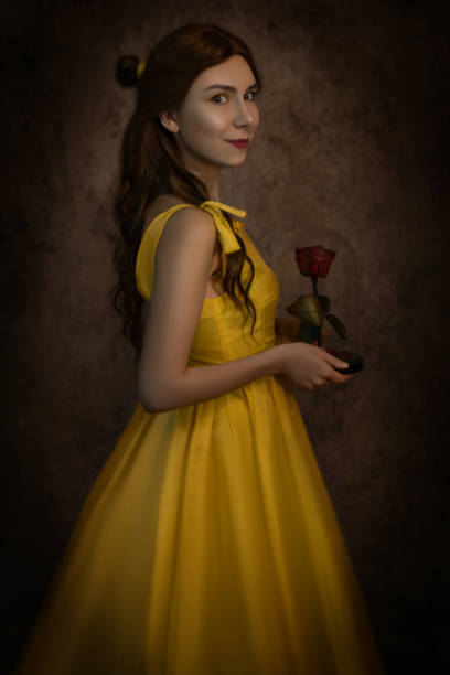 Pretty woman in the yellow long dress closeup with red rose in her hands. Beauty and the beast cosplay Pretty woman in the yellow long dress closeup with red rose in her hands. Beauty and the beast cosplay. beauty and beast rose stock pictures, royalty-free photos & images