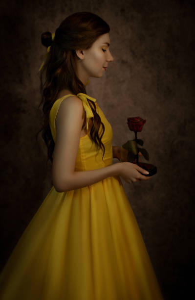 Pretty woman in the yellow long dress closeup with red rose in her hands. Beauty and the beast cosplay Pretty woman in the yellow long dress closeup with red rose in her hands. Beauty and the beast cosplay. beauty and beast rose stock pictures, royalty-free photos & images