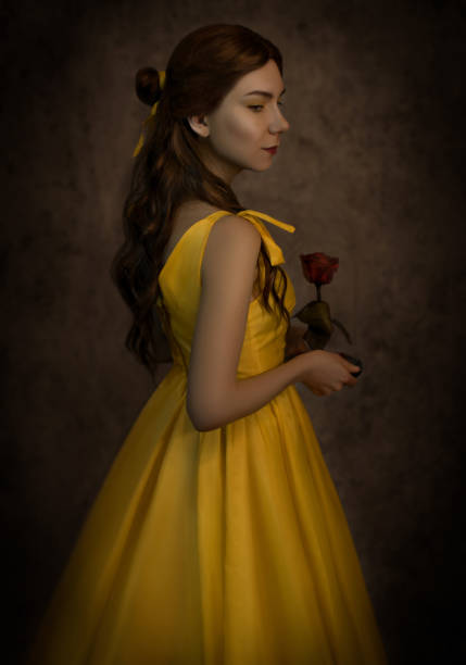 Pretty woman in the yellow long dress closeup with red rose in her hands. Beauty and the beast cosplay Pretty woman in the yellow long dress closeup with red rose in her hands. Beauty and the beast cosplay. beauty and beast rose stock pictures, royalty-free photos & images