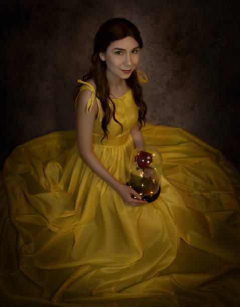 Pretty woman in the yellow long dress closeup with red rose in her hands. Beauty and the beast cosplay Pretty woman in the yellow long dress closeup with red rose in her hands. Beauty and the beast cosplay. beauty and beast rose stock pictures, royalty-free photos & images
