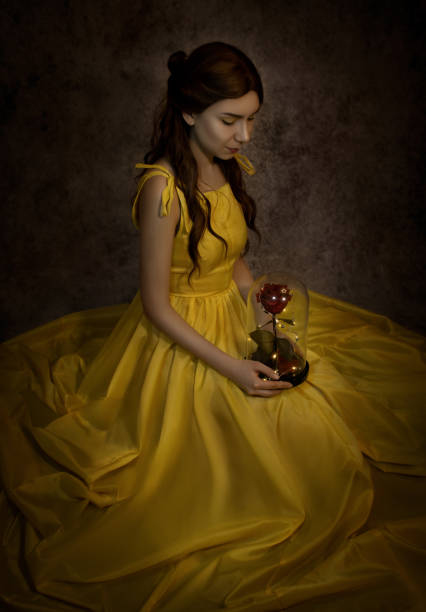 Pretty woman in the yellow long dress closeup with red rose in her hands. Beauty and the beast cosplay Pretty woman in the yellow long dress closeup with red rose in her hands. Beauty and the beast cosplay. beauty and beast rose stock pictures, royalty-free photos & images