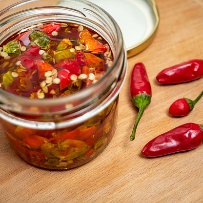 jar with preserved red hot chilly peppers and peppers near on wooden slate