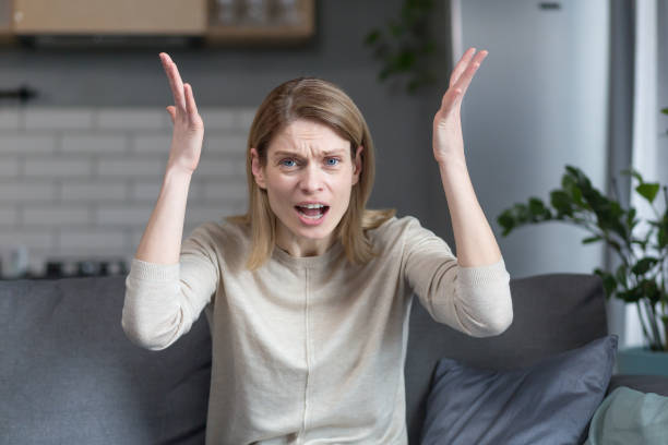 femme en colère et frustrée parlant lors d’un appel vidéo en regardant la webcam, faisant des gestes de colère avec les mains tout en étant assise sur un canapé à la maison - furious photos et images de collection