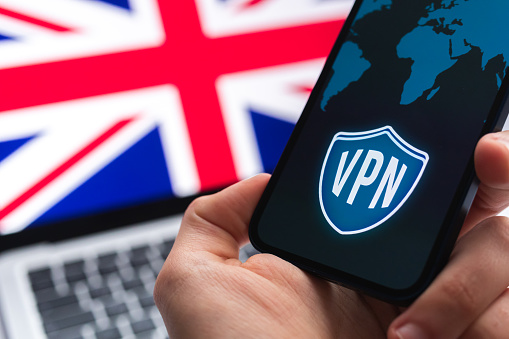 VPN in United Kingdom. Secure and safe internet concept. Privacy. Hand with mobile phone and VPN application. Flag and laptop on the background photo