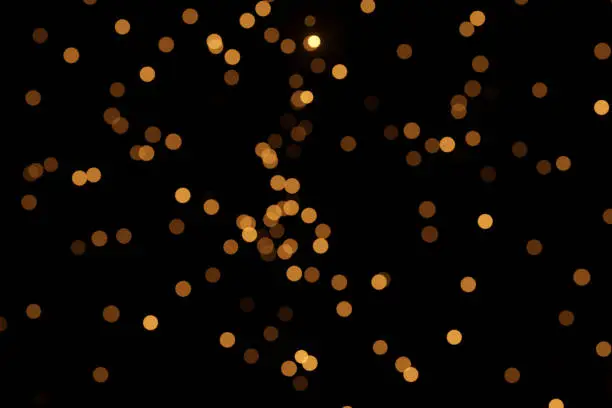 Defocused bokeh lights on black background, an abstract naturally blurred backdrop for Christmas eve or birthday party. Festive light texture. Yellow and red garland in blur. Overlay effect for design