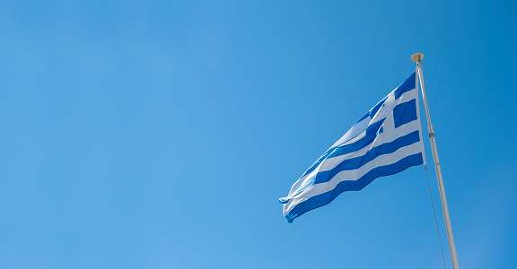 Blue and white colored Greek national flag moving in wind. Beautiful blue clear sky and flag poster background with large copy space. Greece country symbol.