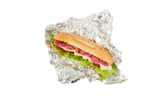 Close up selective focus color image depicting the personal perspective of someone holding a take out box containing a toasted sandwich filled with crispy bacon, melted cheese and fresh salad. Focus is on the delicious fresh sandwich - the person's lunch, bought from a food market - while the city street is defocused beyond.