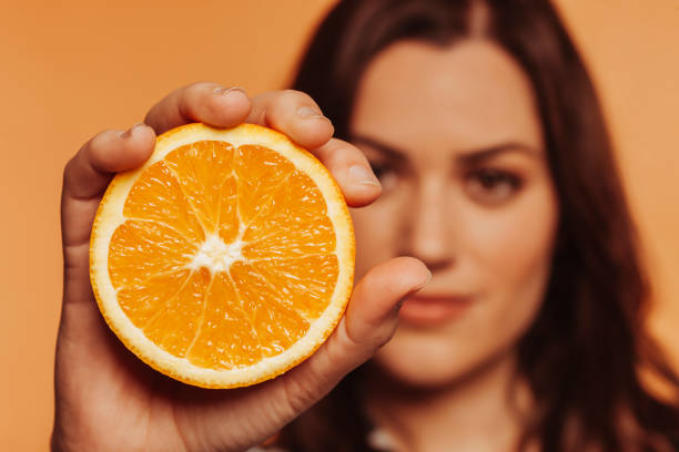 スタジオでオレンジ色を握る女性のクローズアップ肖像画 - close up women horizontal citrus fruit ストックフォトと画像