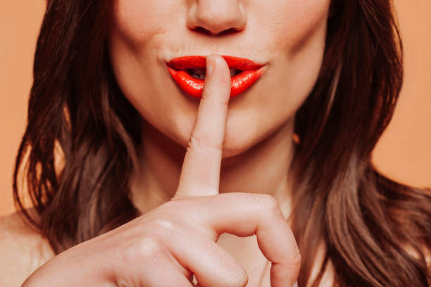 Brunette woman with red lips doing silence gesture with finger