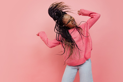 Studio shot of young excited girl with afro hairdo in casual style outfit having fun isolated on pink background. Concept of beauty, art, fashion, youth, style