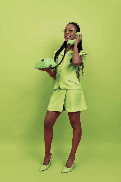 Monochrome portrait of smiling african girl wearing retro style outfit holding vintage phone isolated on green background. Concept of emotions, beauty, art, fashion, youth, style Monochrome portrait of smiling african girl wearing retro style outfit holding vintage phone isolated on green background. Concept of beauty, art, fashion, youth, sales and ads. Copy space for ad. monochrome clothing stock pictures, royalty-free photos & images