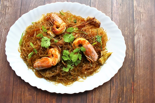 The plate of stir fried noodles with shrimps photo on wooden background top view