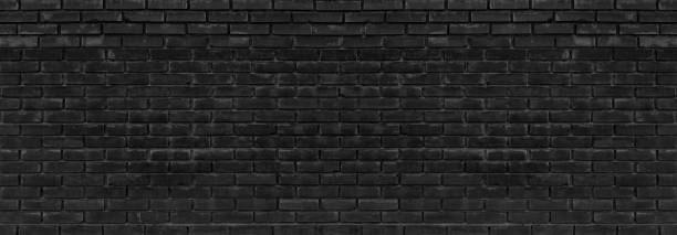 istock Old black messy exterior brick wall wide panoramic texture. Dark gray aged masonry. Grungy brickwork widescreen backdrop. Abstract grunge industrial background 1394169368
