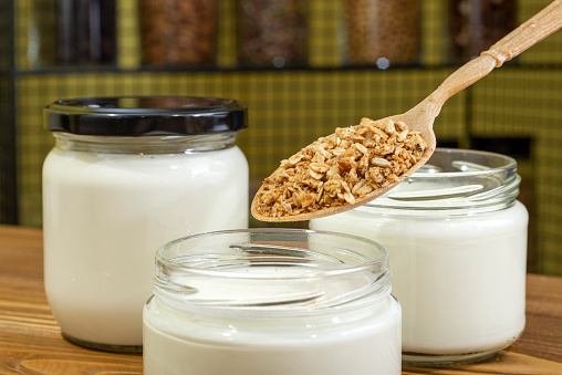 Yogurt in glass jar on a wooden background. Healthy dried fruits and cereals added to yogurt or kefir. Wooden spoon.