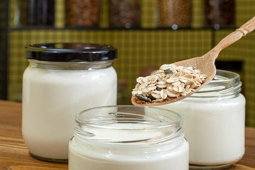 Yogurt in glass jar on a wooden background. Healthy dried fruits and cereals added to yogurt or kefir. Wooden spoon.