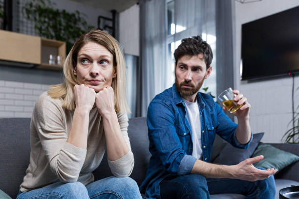 Young family falls apart, depressed woman because of alcoholic husband, couple sitting on sofa in living room Young family falls apart, depressed woman because of alcoholic husband, couple sitting on sofa in living room arguing couple divorce family stock pictures, royalty-free photos & images