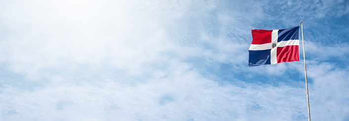 Flying and waving flag of Dominican Republic on wind on blue sky background