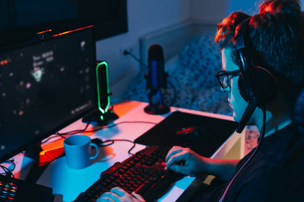istock Young professional online video game player, playing on a computer. Young gamer illuminated with coloured lights. 1394180514