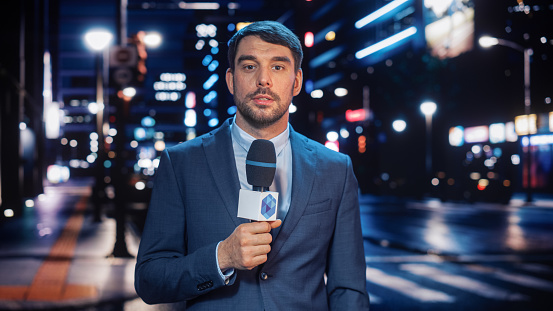 Anchorman Reporting Live News in a City at Night. News Coverage by Professional Handsome Reporter from a Business District. Journalist Presenting News for TV Channel. Newscaster Talking.