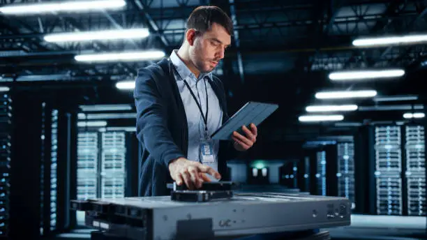 Photo of Successful Data Center IT Specialist Using Tablet Computer. Server Farm Cloud Computing Facility with System Administrator Working. Data Protection Engineering Network for Cyber Security.